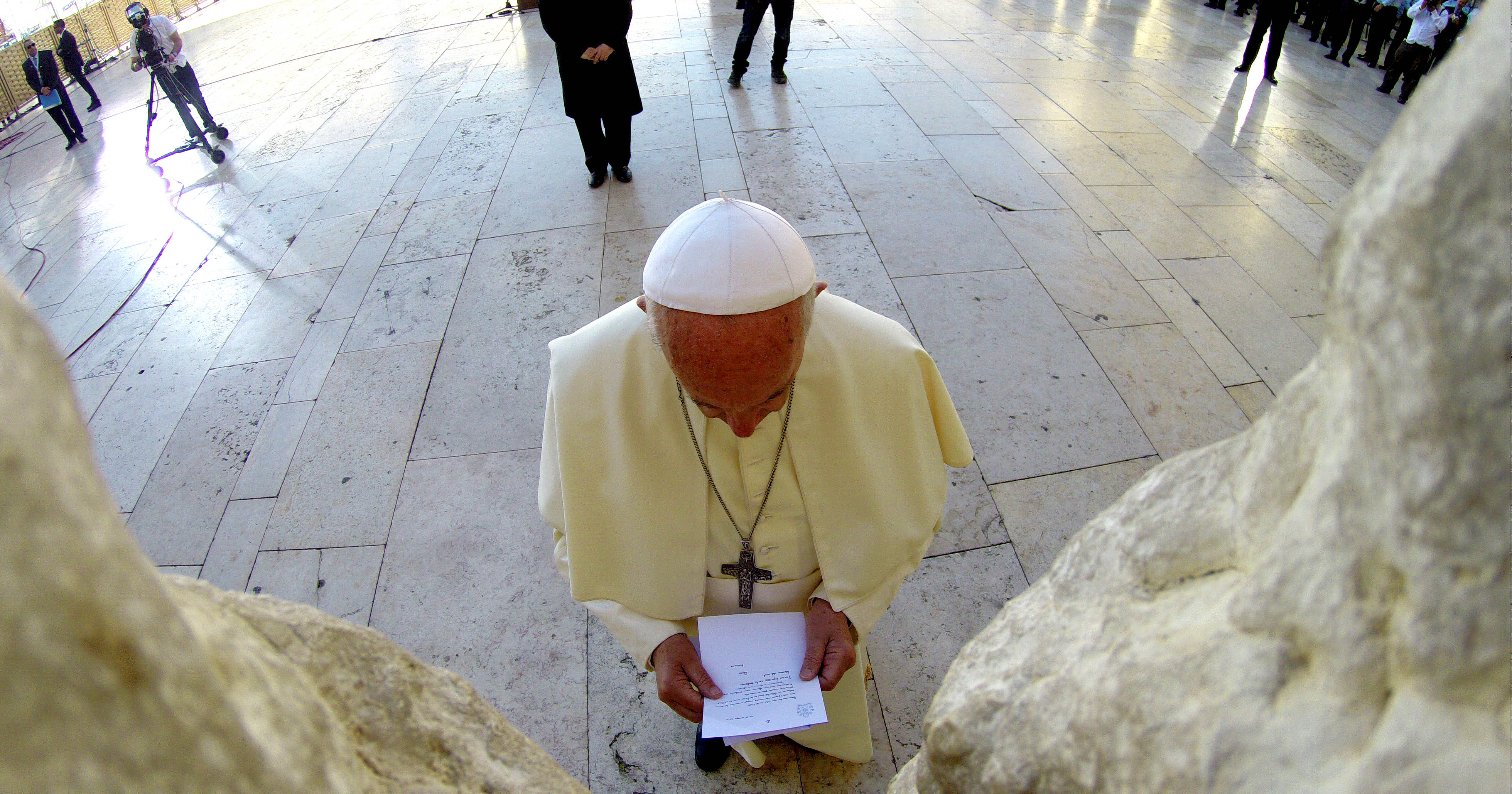 Pope Francis holding his prayer note, viewed from within the stones of the Wall